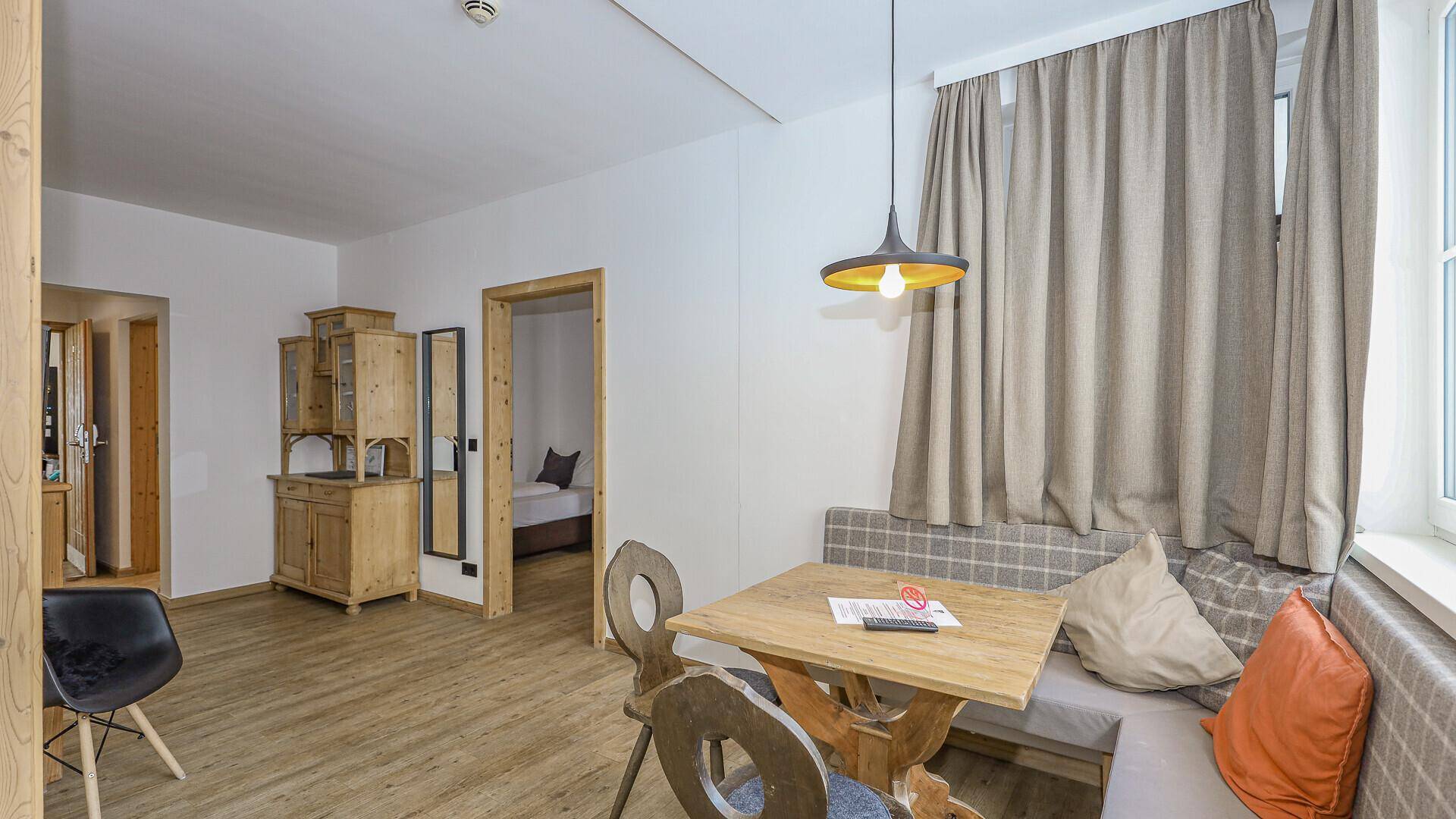 Wohn- und Essbereich mit traditionellen Holzmöbeln, Parkettboden und Zugang zu einem Schlafzimmer.