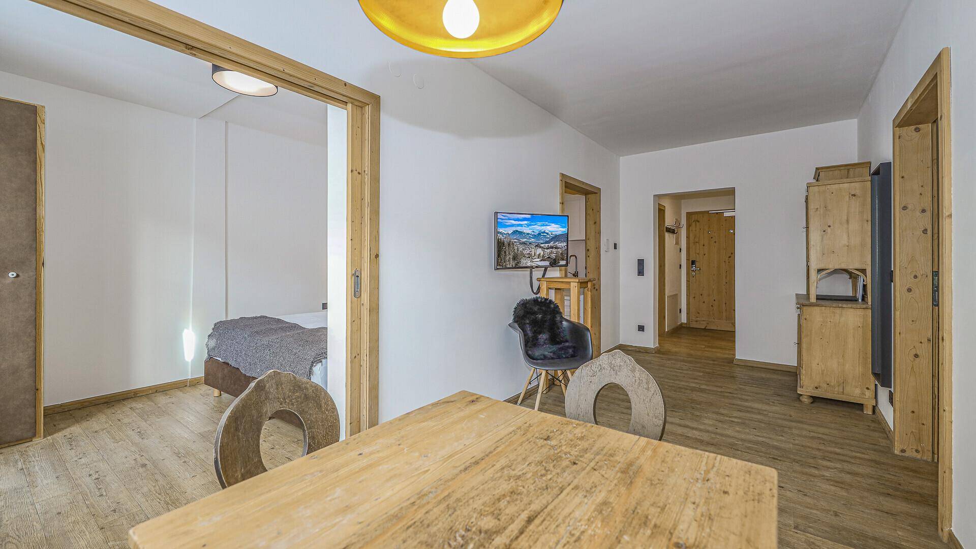 Essbereich mit Holztisch und Blick auf einen Flachbildfernseher sowie Zugang zu einem Schlafzimmer.