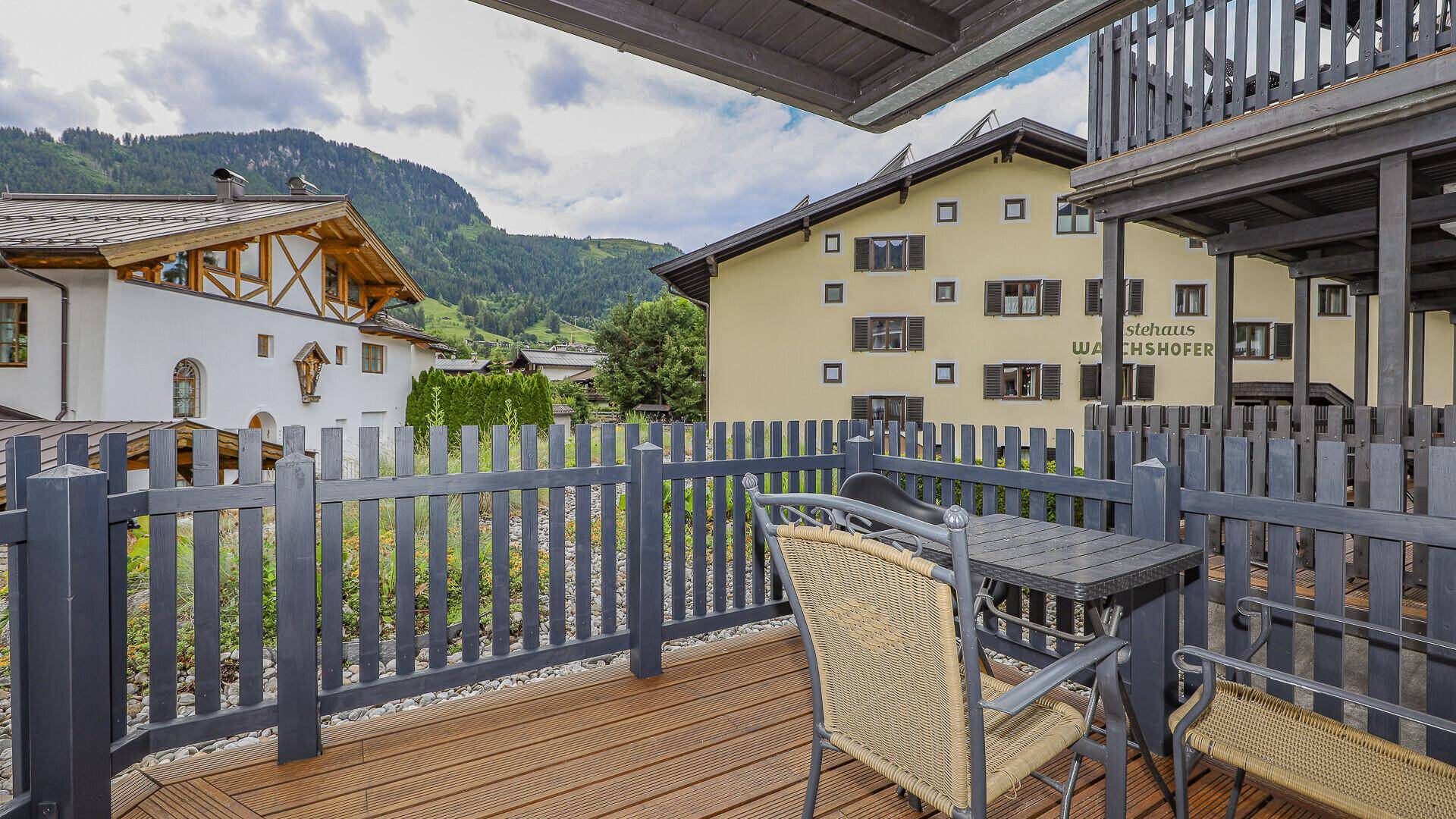 Kleiner Balkon mit Holzboden, Sitzgelegenheiten und Blick auf die umliegenden Häuser.