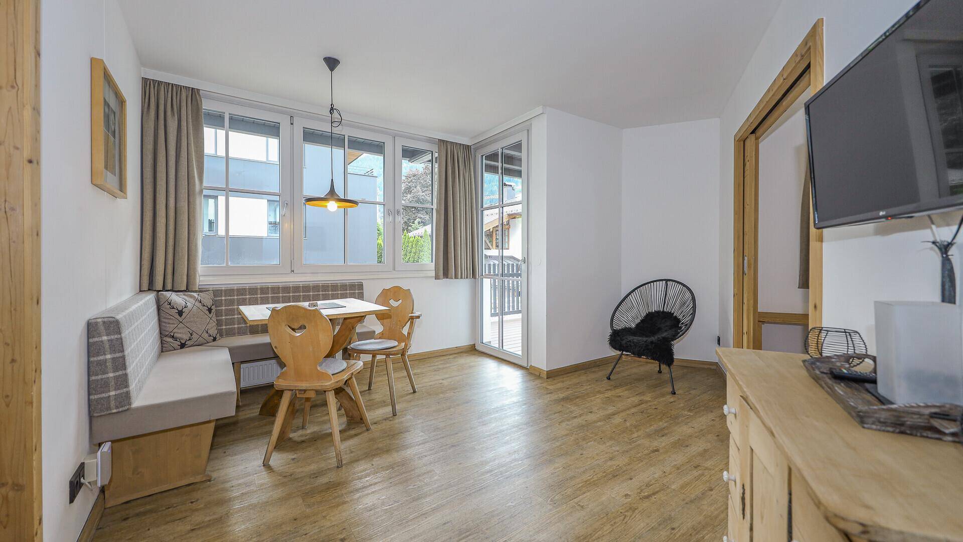 Gemütlicher Wohn-Essbereich mit Holzboden, Sitzbank und Zugang zum Balkon.