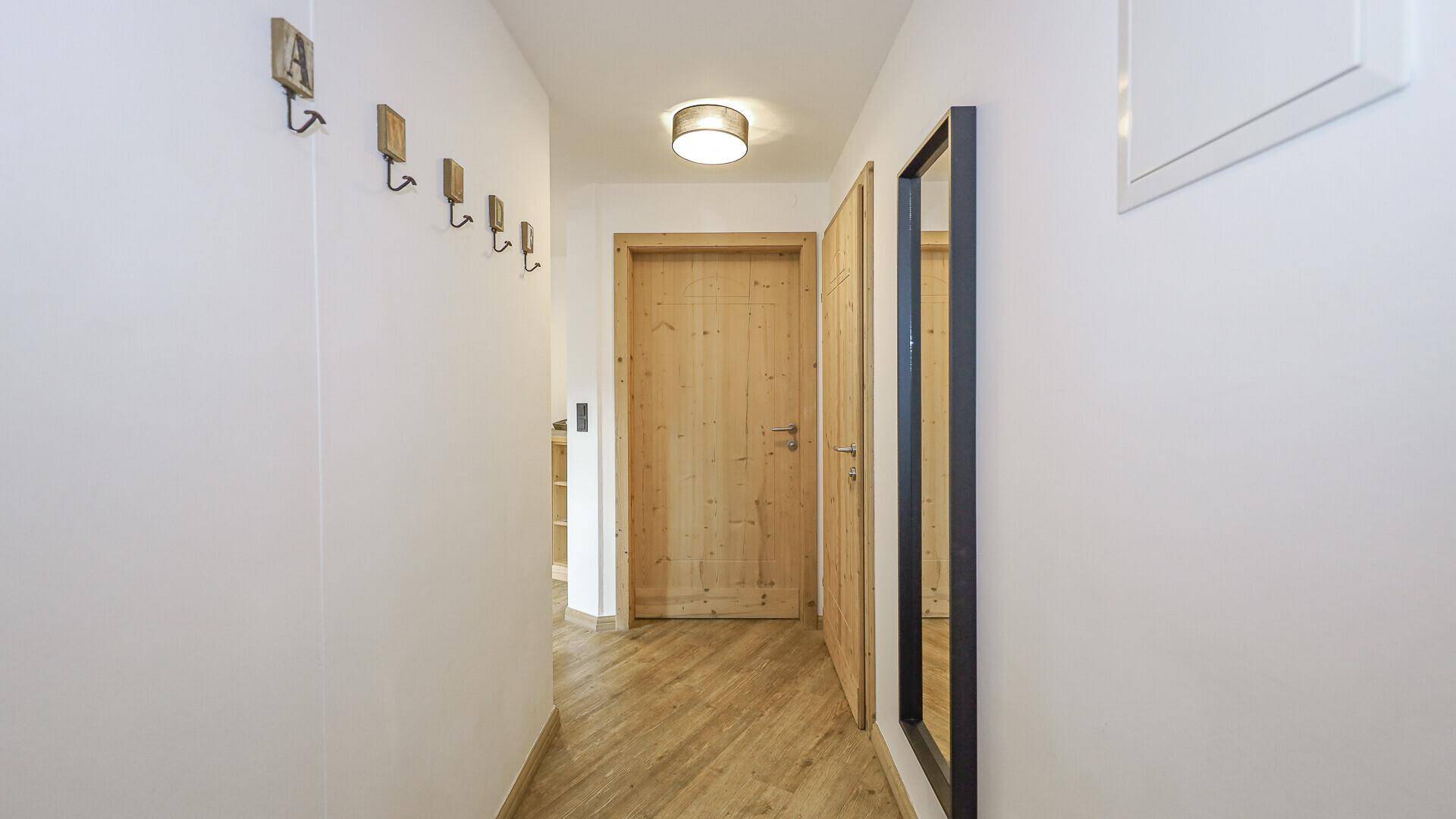 Heller Flur mit Holzboden, Garderobenhaken und Zugang zu weiteren Räumen.