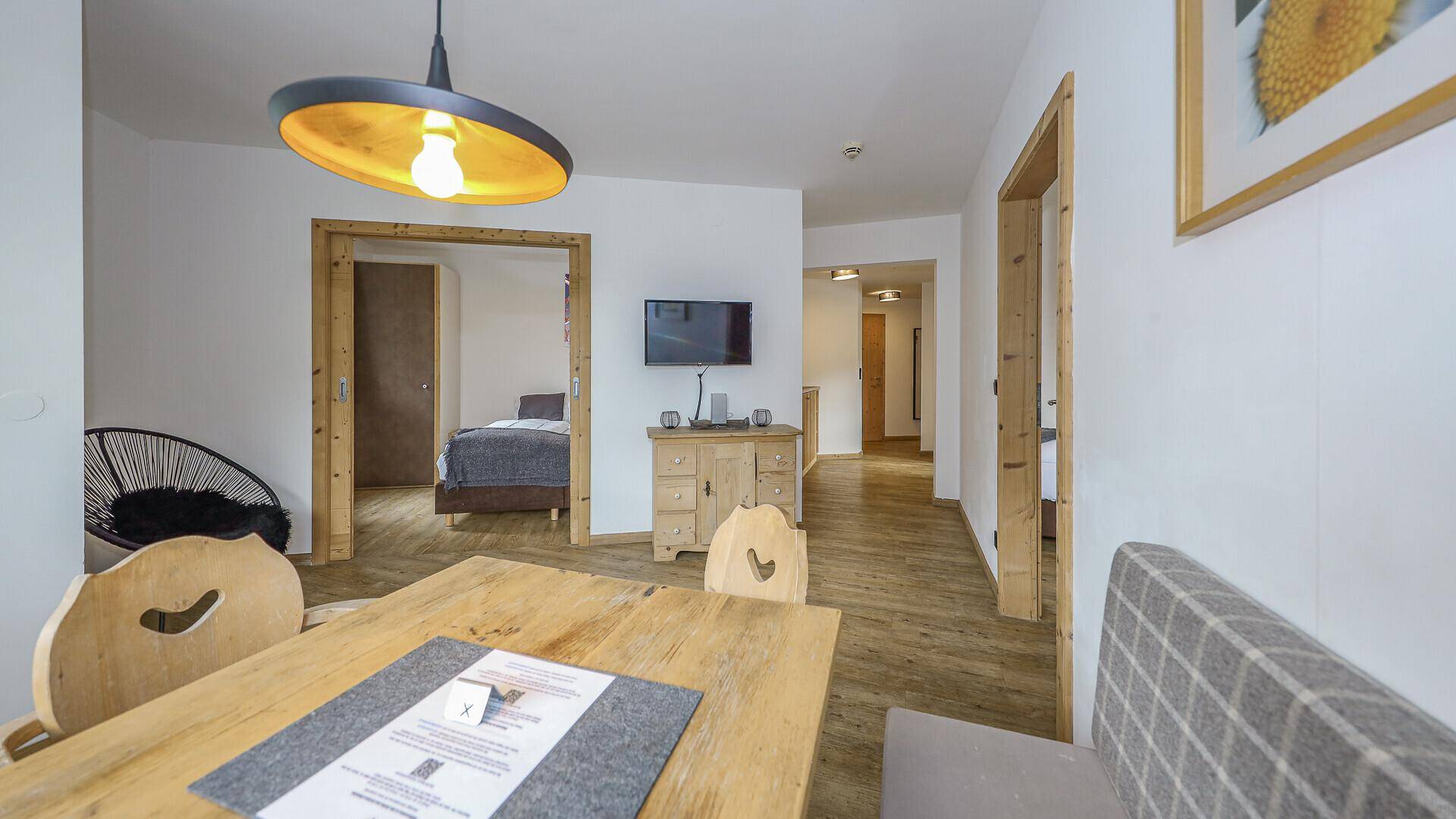 Heller Wohn-Essbereich mit Holztisch und Blick in ein angrenzendes Schlafzimmer.
