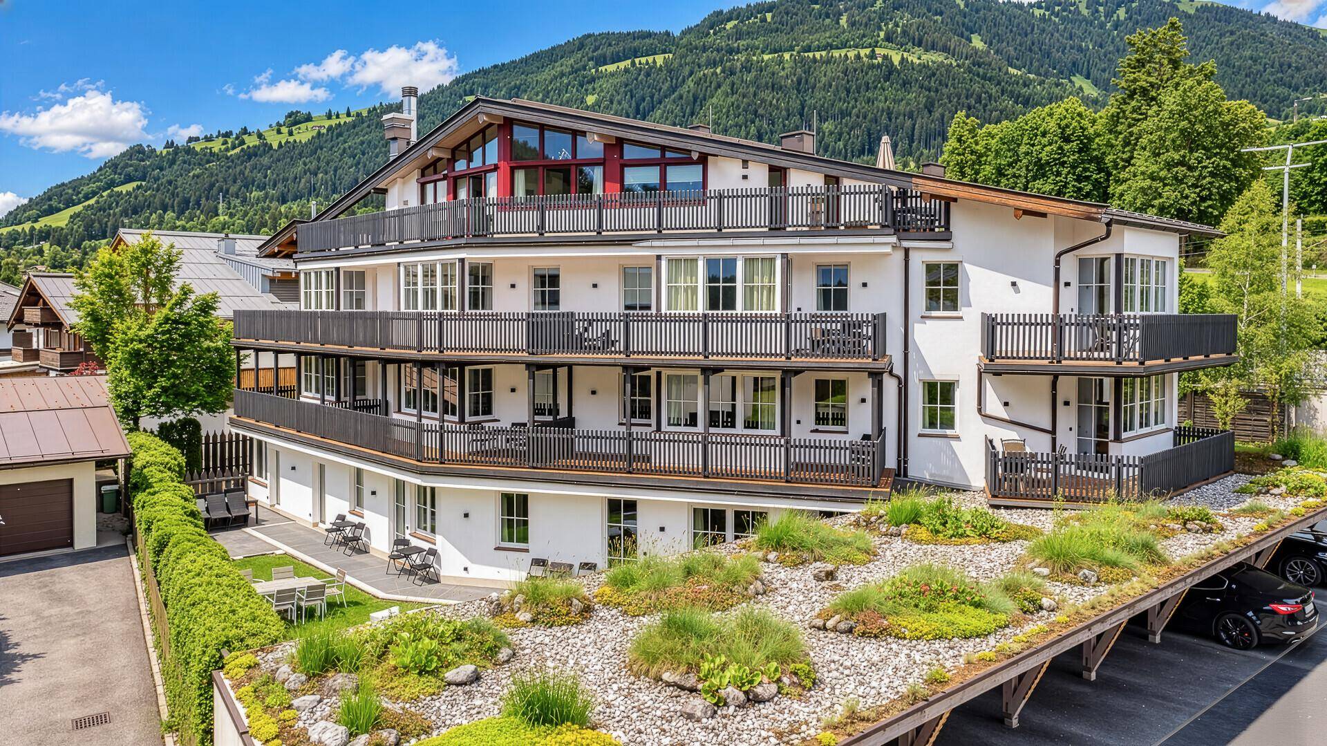 Modernes Mehrfamilienhaus mit mehreren Balkonen und begrüntem Dach in alpiner Umgebung.