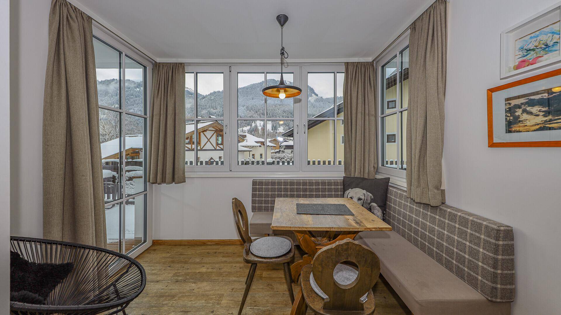 Heller Essbereich mit Holztisch, Sitzbank und Panoramafenstern mit Bergblick.