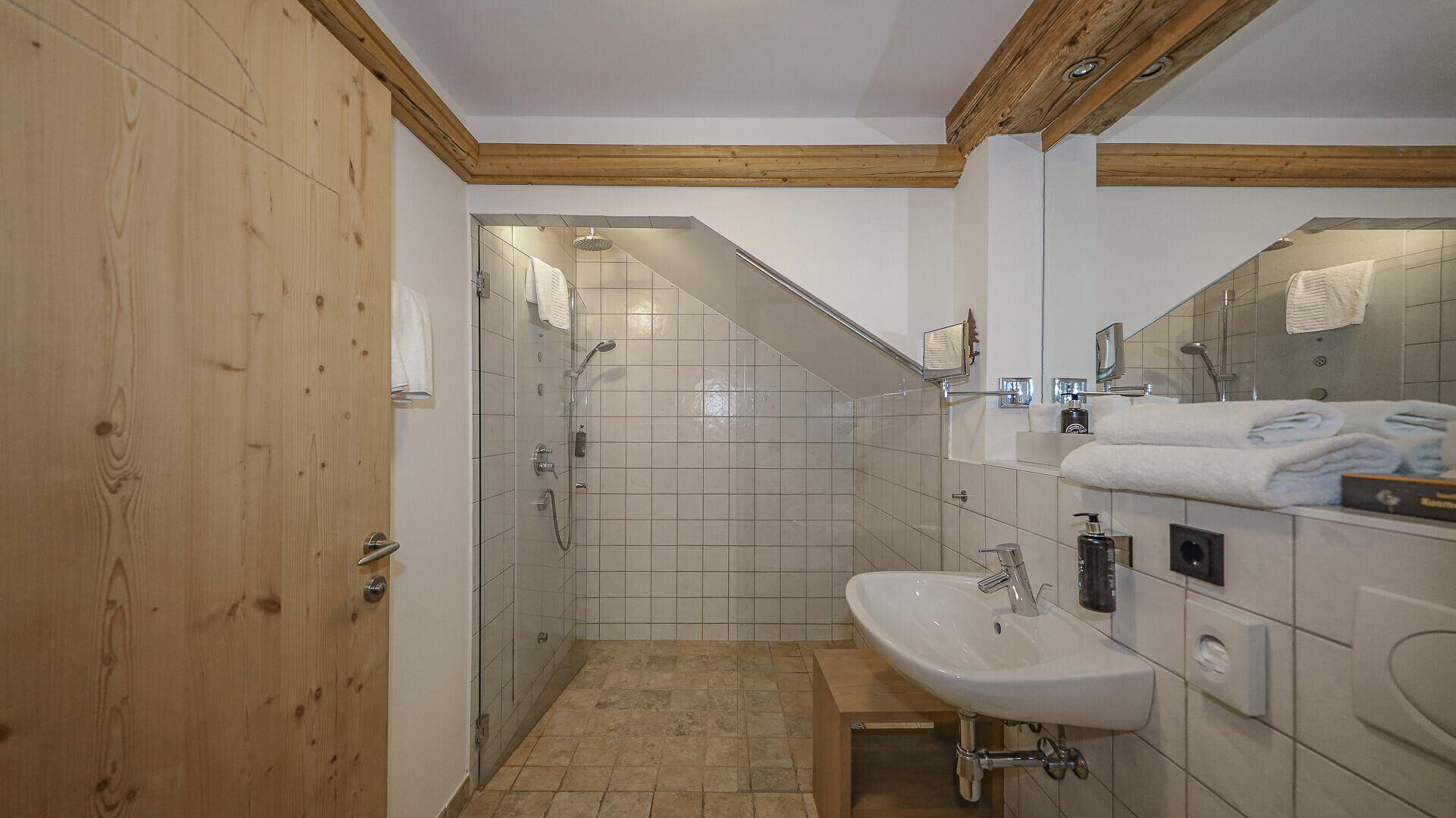 Modernes Badezimmer mit begehbarer Dusche, Einzelwaschbecken und Holzbalken an der Decke.