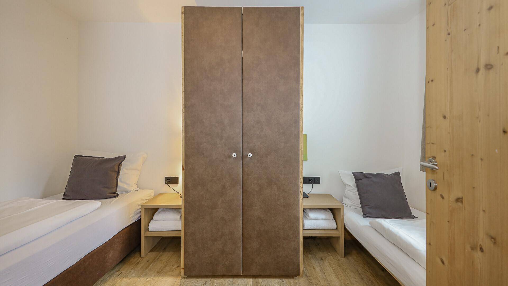 Schlafzimmer mit zwei Einzelbetten und einem Kleiderschrank, funktional eingerichtet.