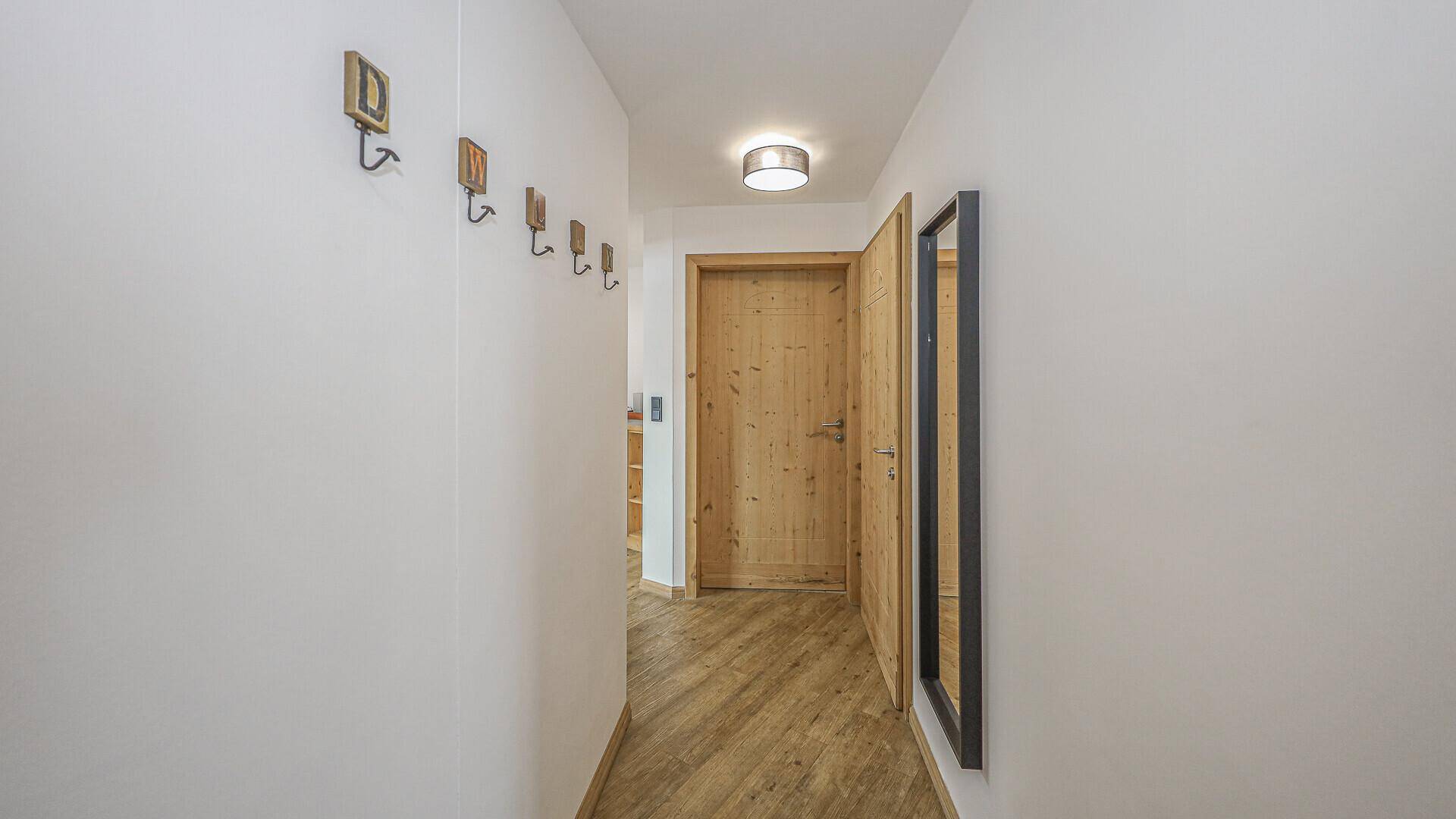 Langer, heller Flur mit Holzboden, Garderobe und einem Spiegel.