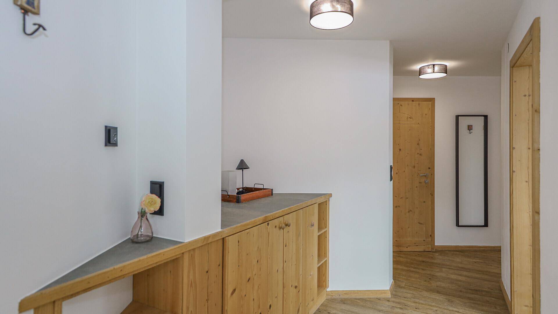 Heller Flur mit Holzmöbeln und Garderobe, der zu weiteren Räumen führt.