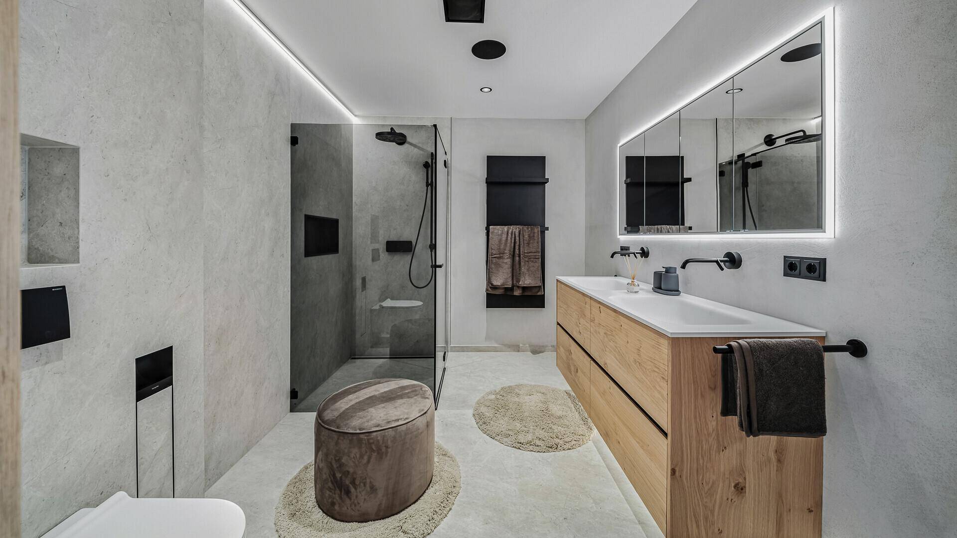 Elegantes Badezimmer mit Doppelwaschbecken, begehbarer Dusche und beleuchtetem Spiegelschrank.