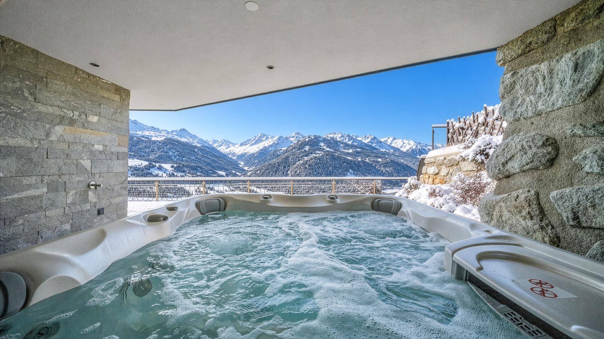 Außen-Whirlpool auf einer Terrasse mit atemberaubendem Blick auf die verschneiten Berge.