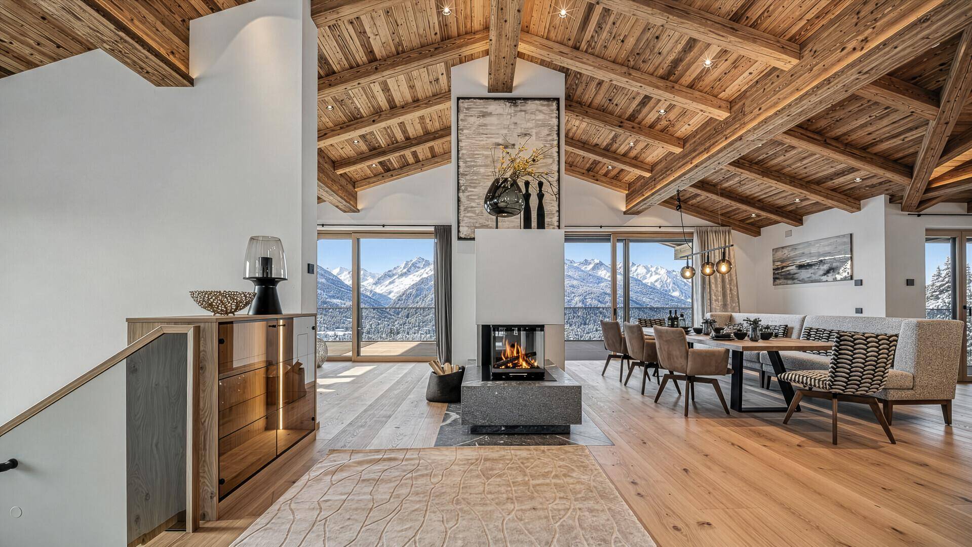 Geräumiger Wohn- und Essbereich mit Holzbalkendecke, Kamin und Panoramablick auf die Berge.