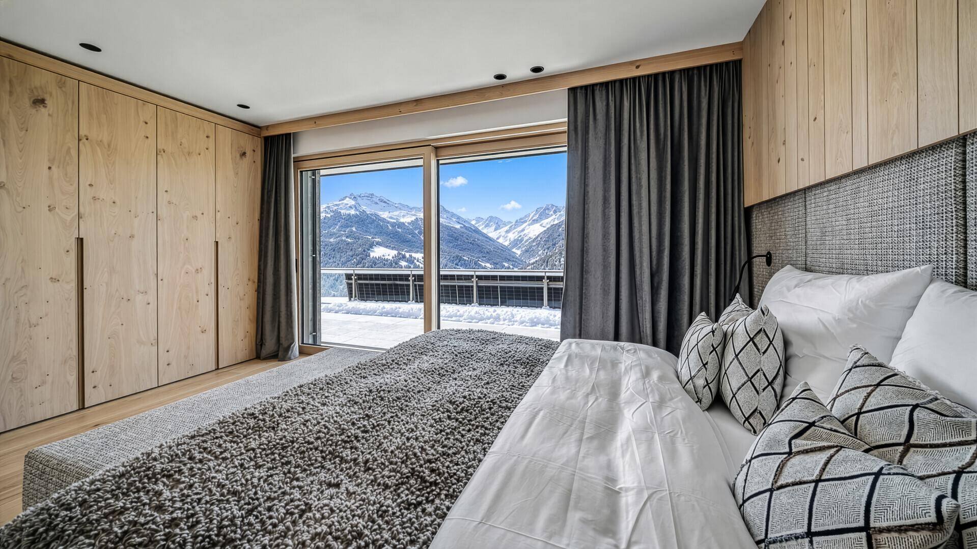 Schlafzimmer mit Einbauschränken, Holzwand und Balkonzugang mit Bergblick.