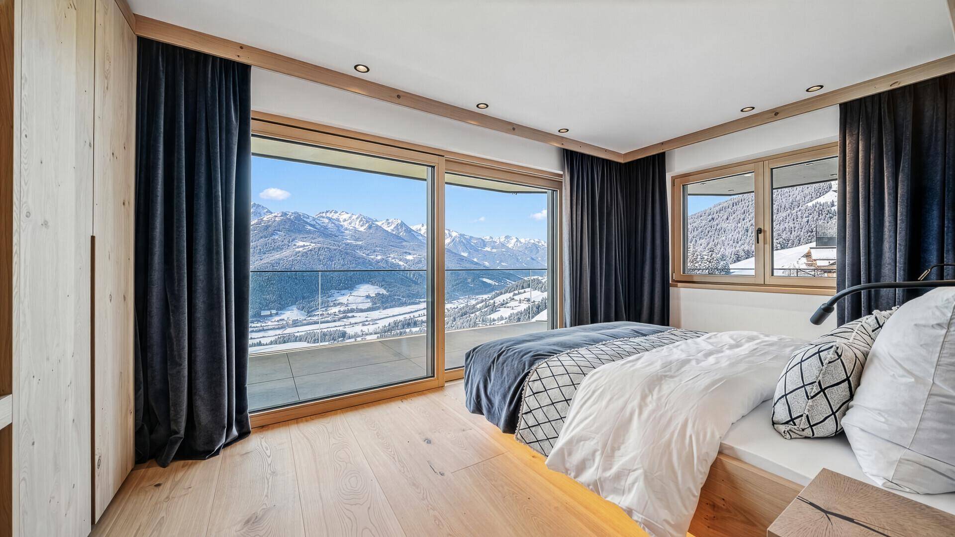 Helles Schlafzimmer mit Holzboden, großem Fenster und atemberaubendem Blick auf die verschneiten Berge.