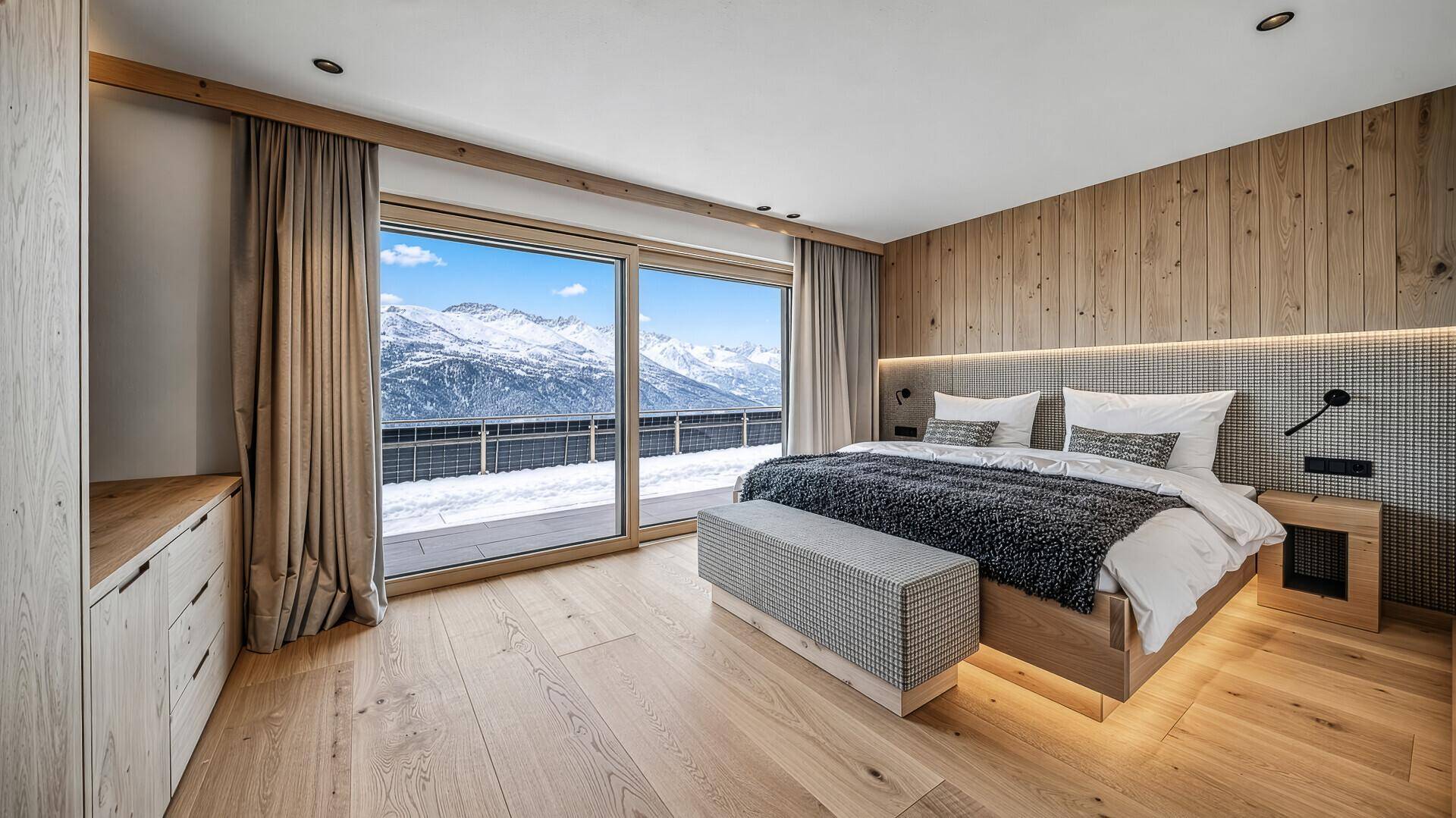 Schlafzimmer mit Holzwand, großem Bett und direktem Zugang zu einem Balkon mit Bergblick.