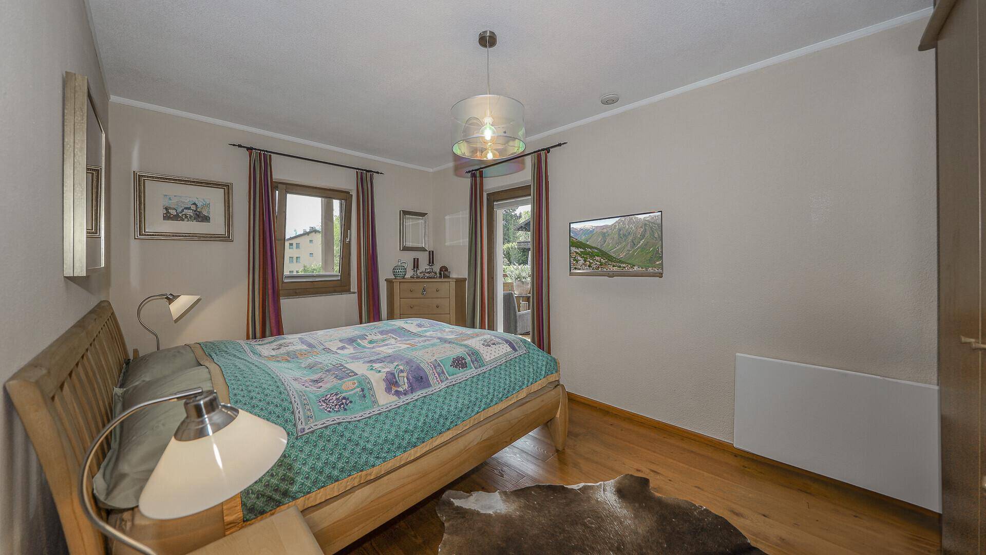 Gemütliches Schlafzimmer mit Holzbett, Fernseher und Zugang zu einem Balkon.