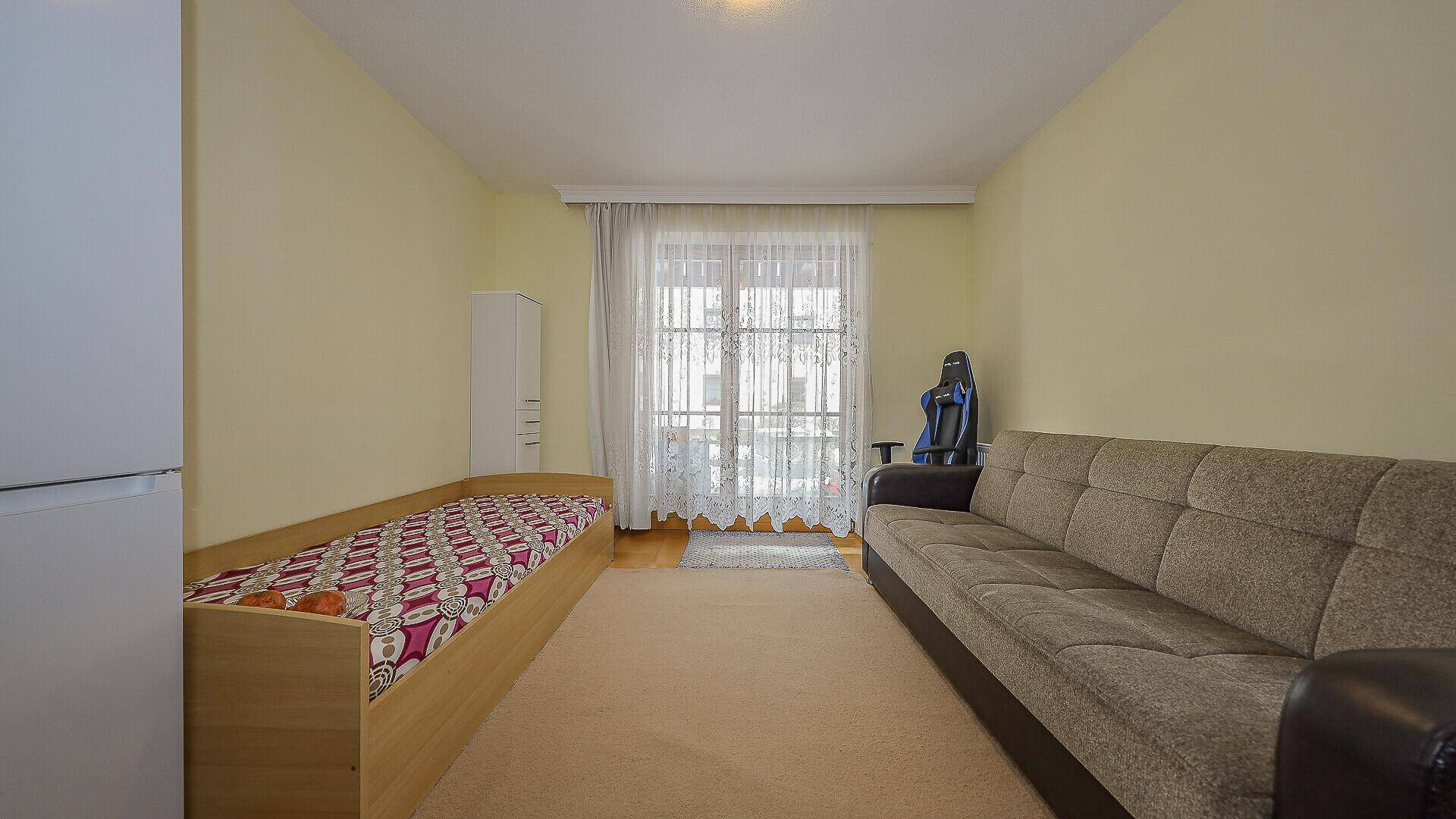 Gemütliches Zimmer mit Einzelbett, Sofa und hellem Fenster.