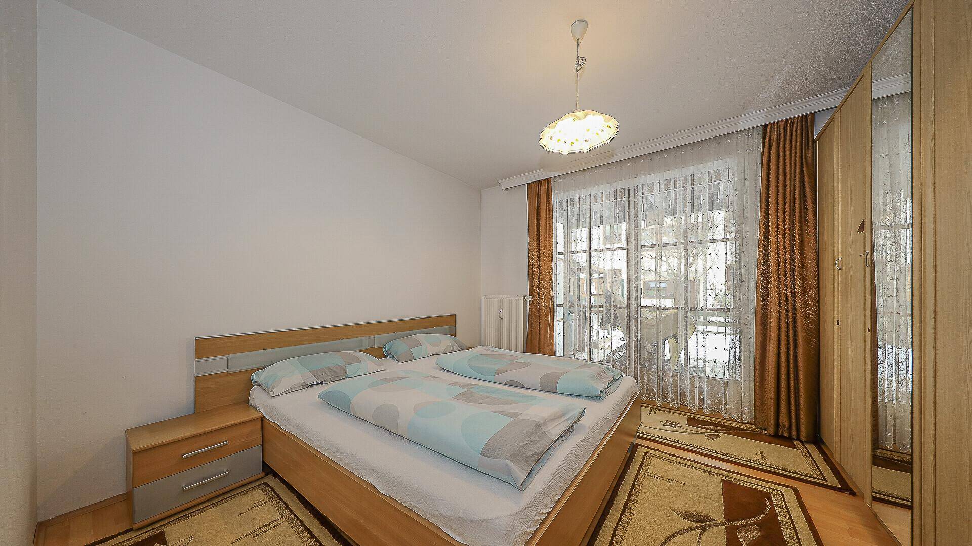 Helles Schlafzimmer mit Doppelbett, Kleiderschrank und Zugang zu einem Balkon.