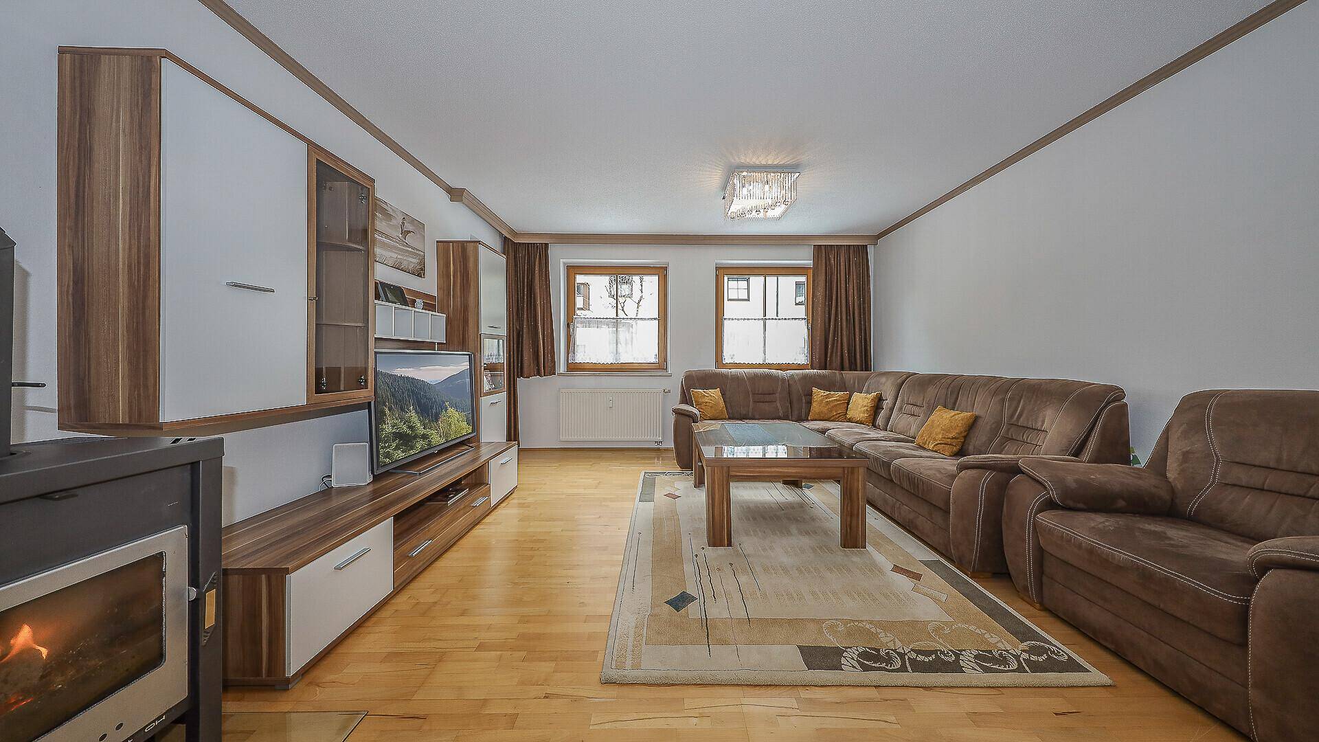 Geräumiges Wohnzimmer mit bequemer Sitzecke, Holzboden und einem wärmenden Kaminofen.