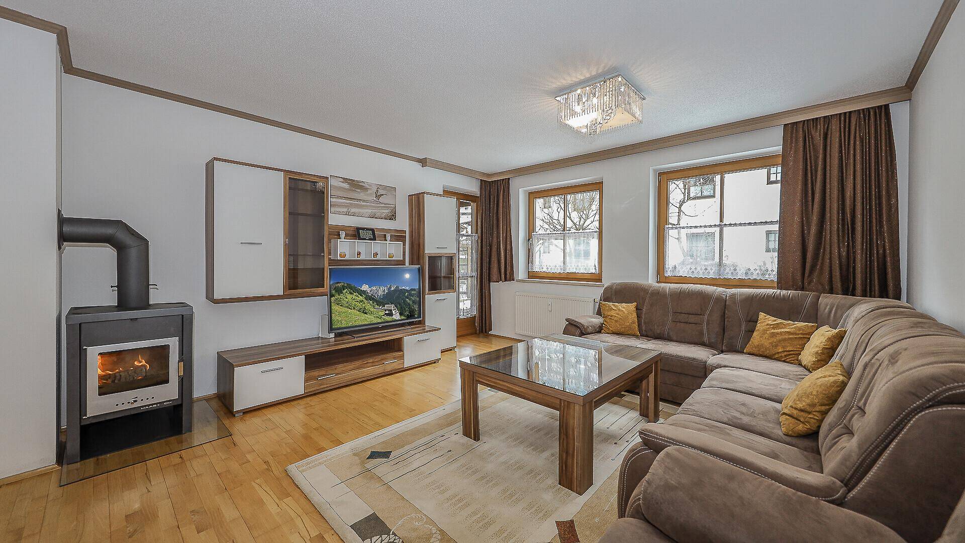 Gemütliches Wohnzimmer mit braunem Sofa, Holzboden und einem modernen Kaminofen.