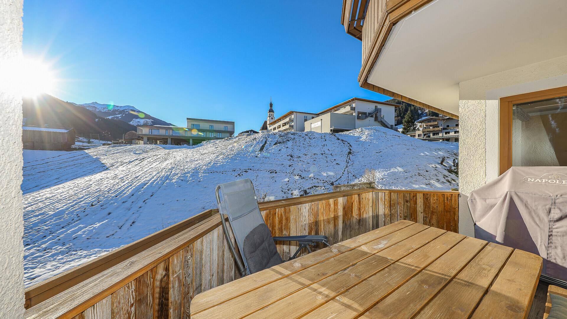 Geräumiger Balkon mit Holzboden, Grill und Panoramablick auf die winterliche Berglandschaft.