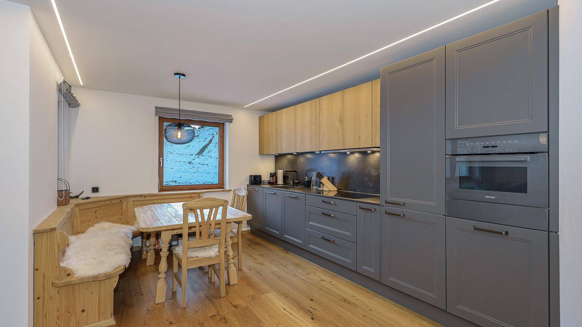 Moderne Küche mit grauen und holzfarbenen Schränken sowie einem gemütlichen Essbereich mit Eckbank.
