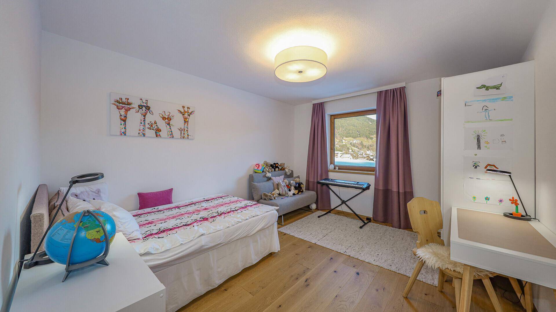 Kinderzimmer mit Einzelbett, Schreibtisch und Fenster, dekoriert mit bunten Elementen.