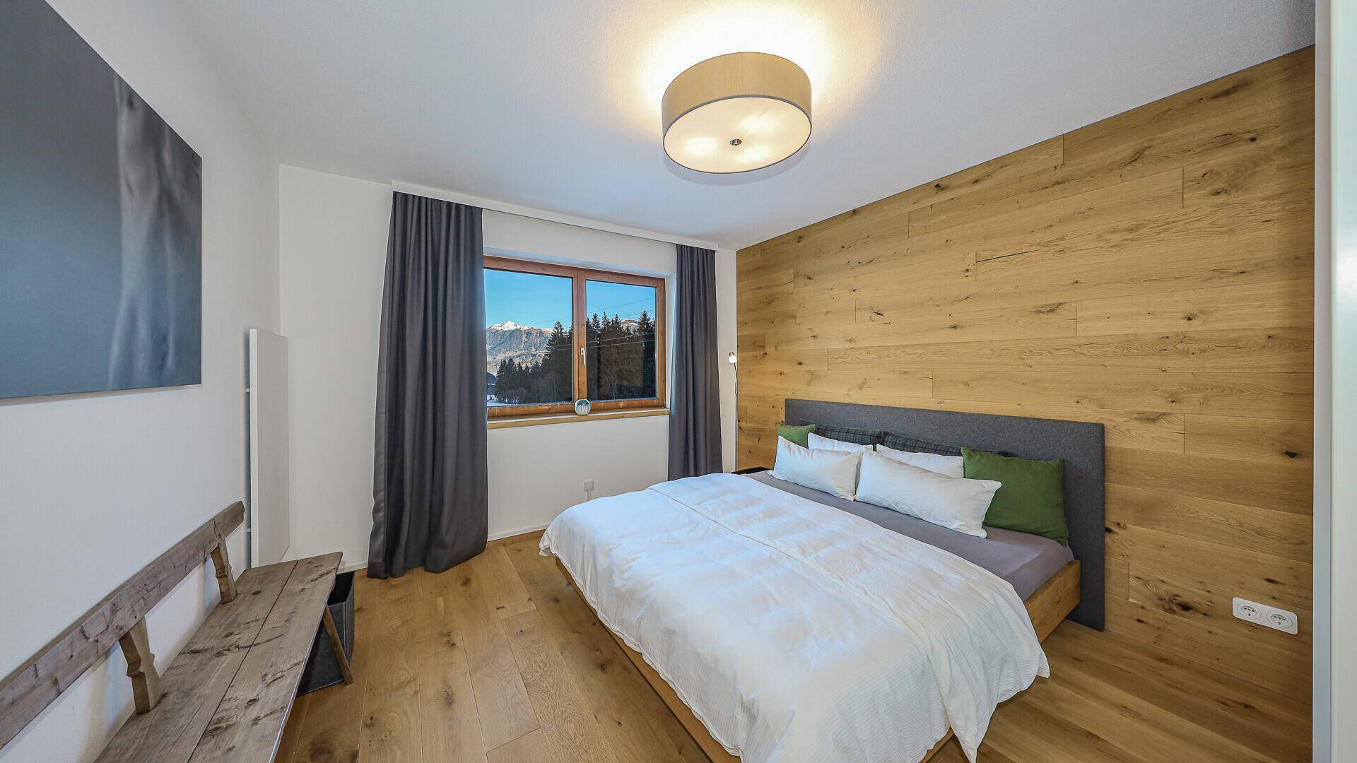 Gemütliches Schlafzimmer mit Holzwand, Doppelbett und Fenster mit Blick auf die Berge.