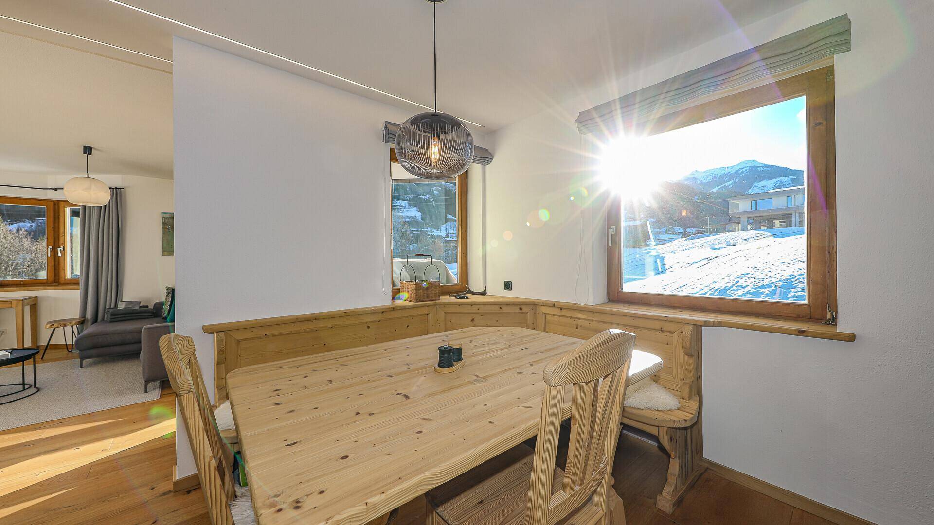 Heller Essbereich mit Holztisch und Eckbank, durchflutet von Sonnenlicht mit Bergblick.