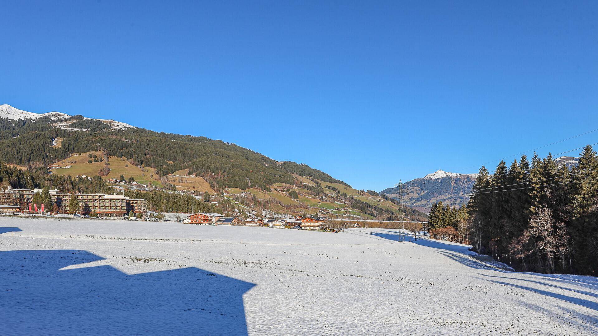 Weite, verschneite Landschaft mit sanften Hügeln und Bergen unter klarem blauem Himmel.
