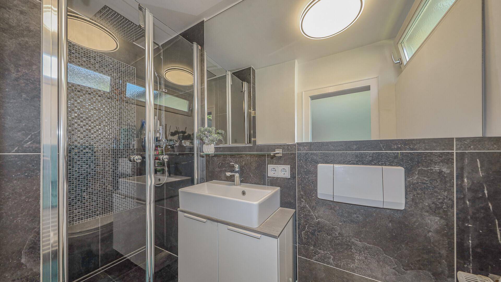 Modernes Badezimmer mit Dusche, Waschbecken und dunklen Fliesen.