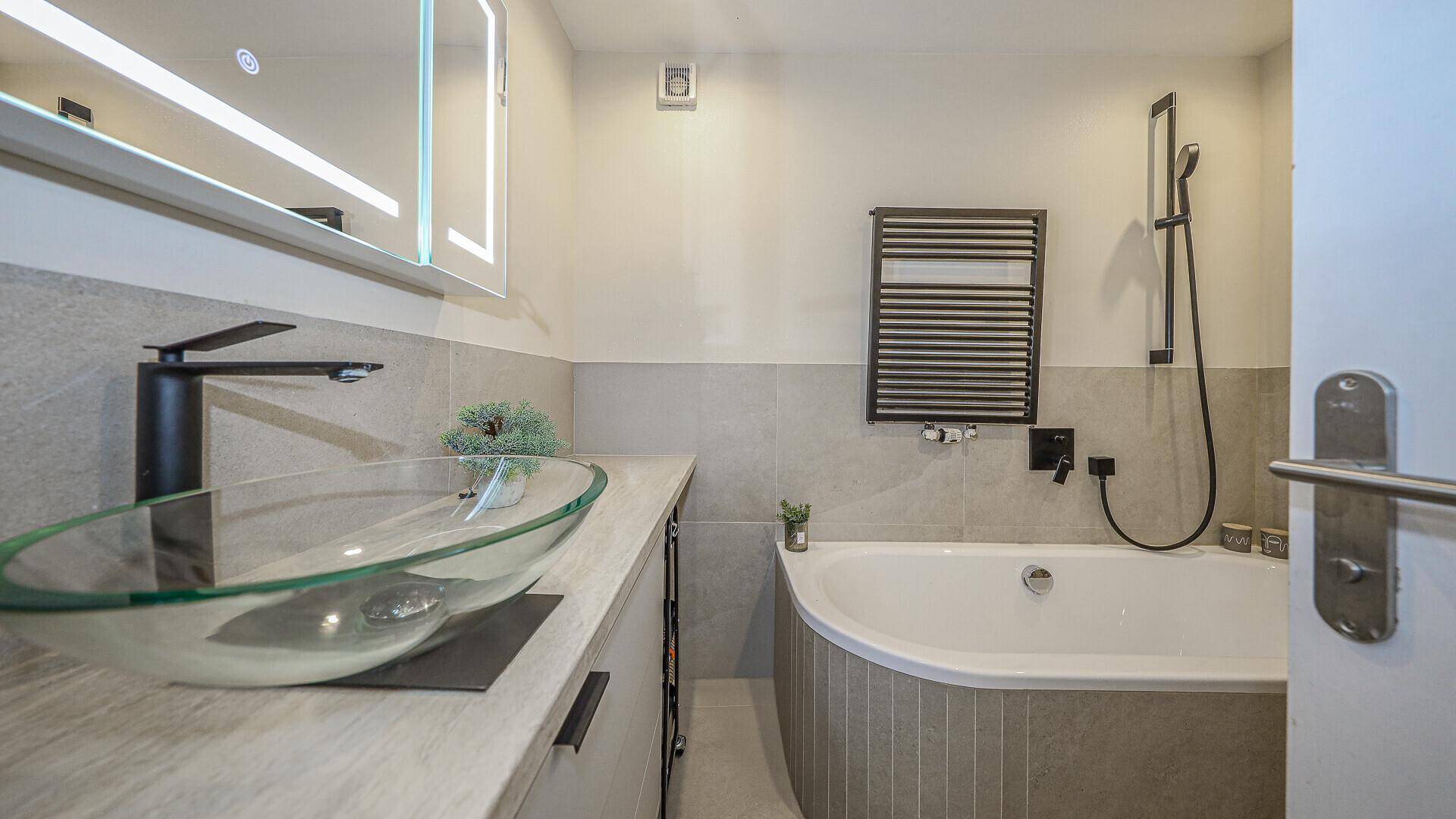 Modernes Badezimmer mit Badewanne, Glaswaschbecken und beheiztem Handtuchhalter.
