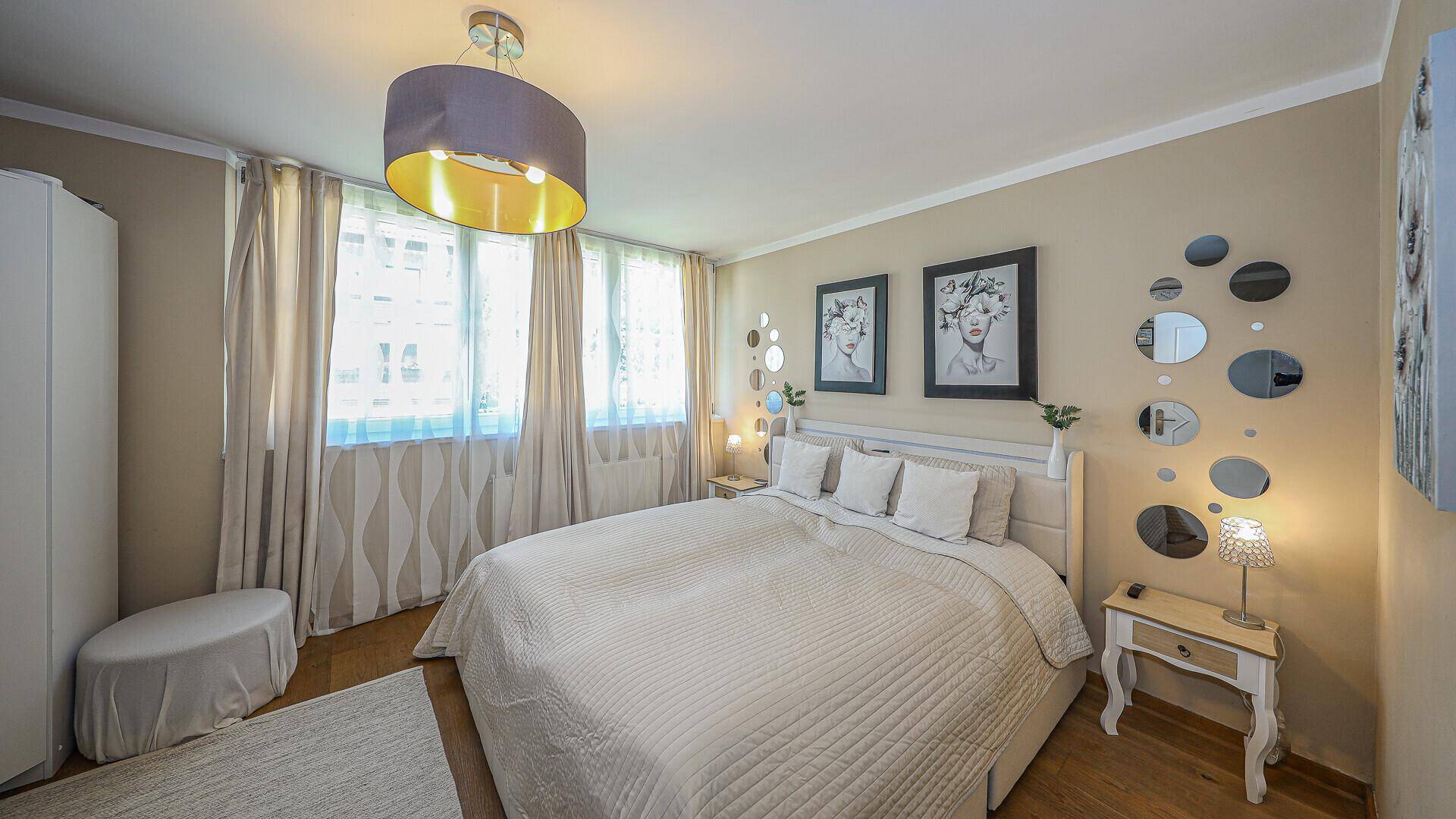 Helles Schlafzimmer mit Doppelbett, Holzboden und großen Fenstern.