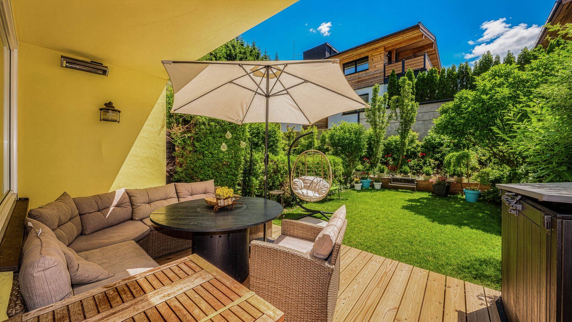 Sonniger Außenbereich mit möblierter Terrasse, Rasenfläche und Garten.