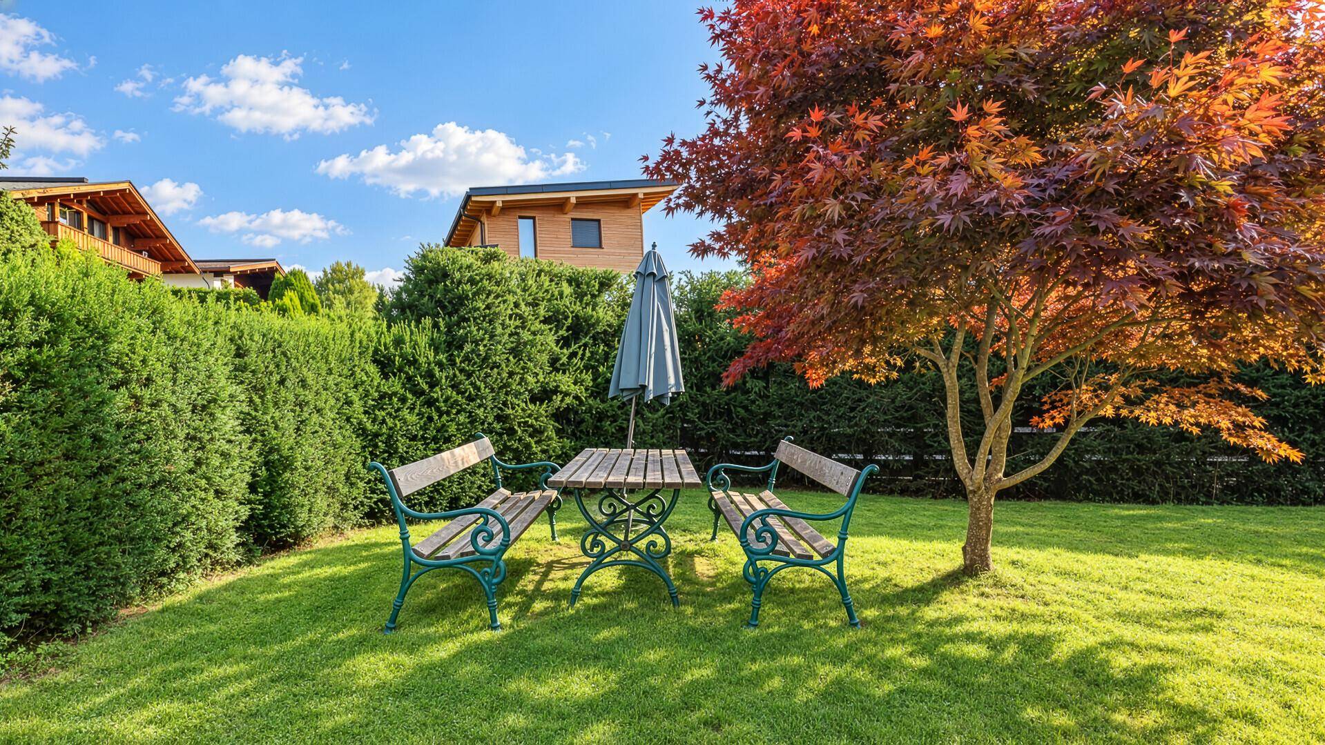 Gepflegter Garten mit Rasenfläche, Sitzgruppe und schattenspendendem Baum.