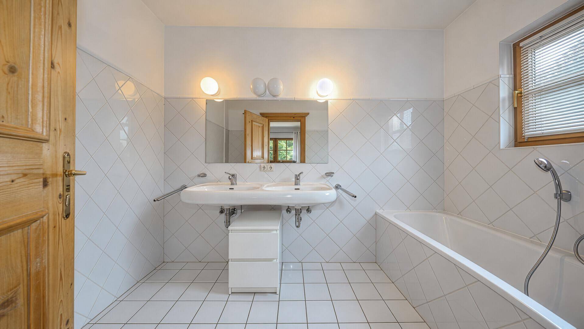 Geräumiges Badezimmer mit Doppelwaschbecken, Badewanne und weißen Fliesen.
