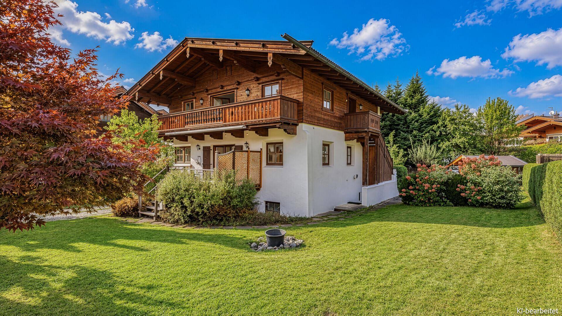 Charmantes Holzchalet mit gepflegtem Rasen und herbstlichem Baum vor blauem Himmel.