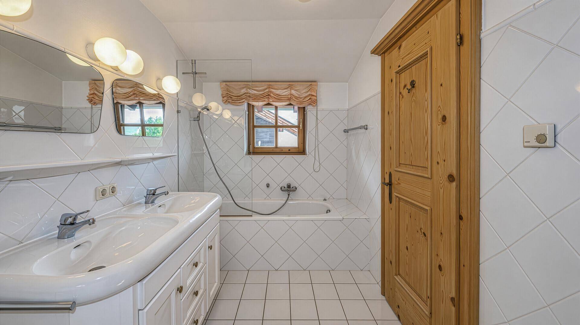 Badezimmer mit Doppelwaschbecken, Badewanne und weißen Fliesen.