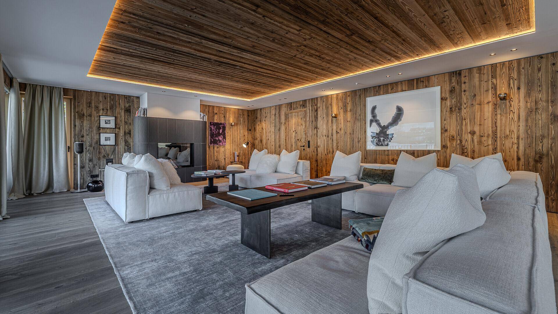 Gemütlicher Wohnbereich mit Holzwänden, Kamin und bequemen Sofas in modernem Chalet-Stil.
