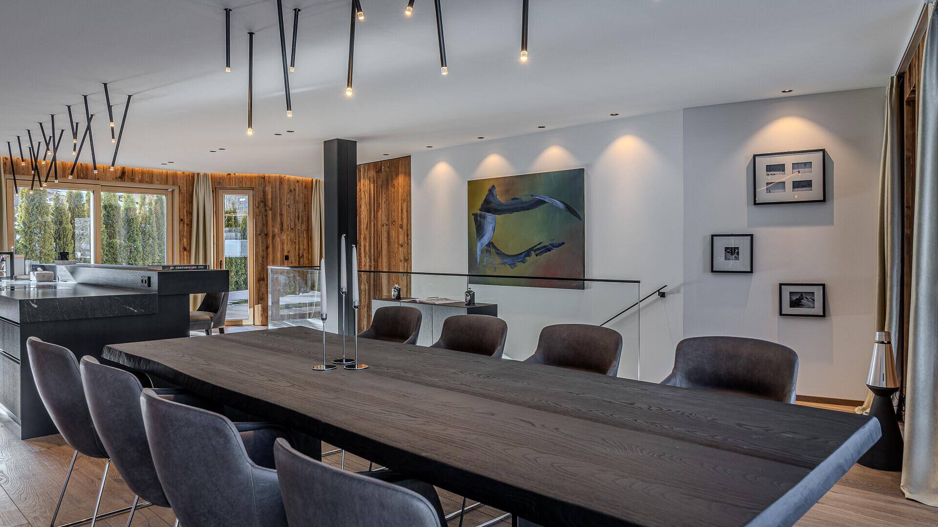 Eleganter Essbereich mit großem Holztisch, modernen Hängelampen und Kunstwerken an der Wand.