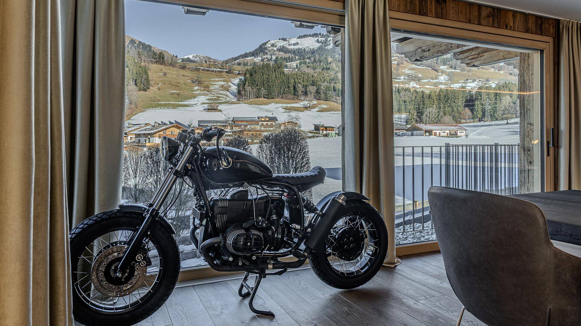 Große Fensterfront mit Blick auf die verschneite Berglandschaft und ein stilvolles Motorrad als Dekoration.