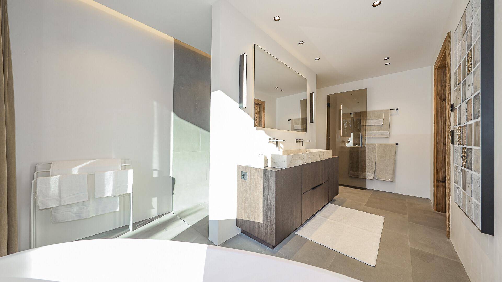 Modernes Badezimmer mit freistehender Badewanne, Doppelwaschbecken und großen Fliesen.