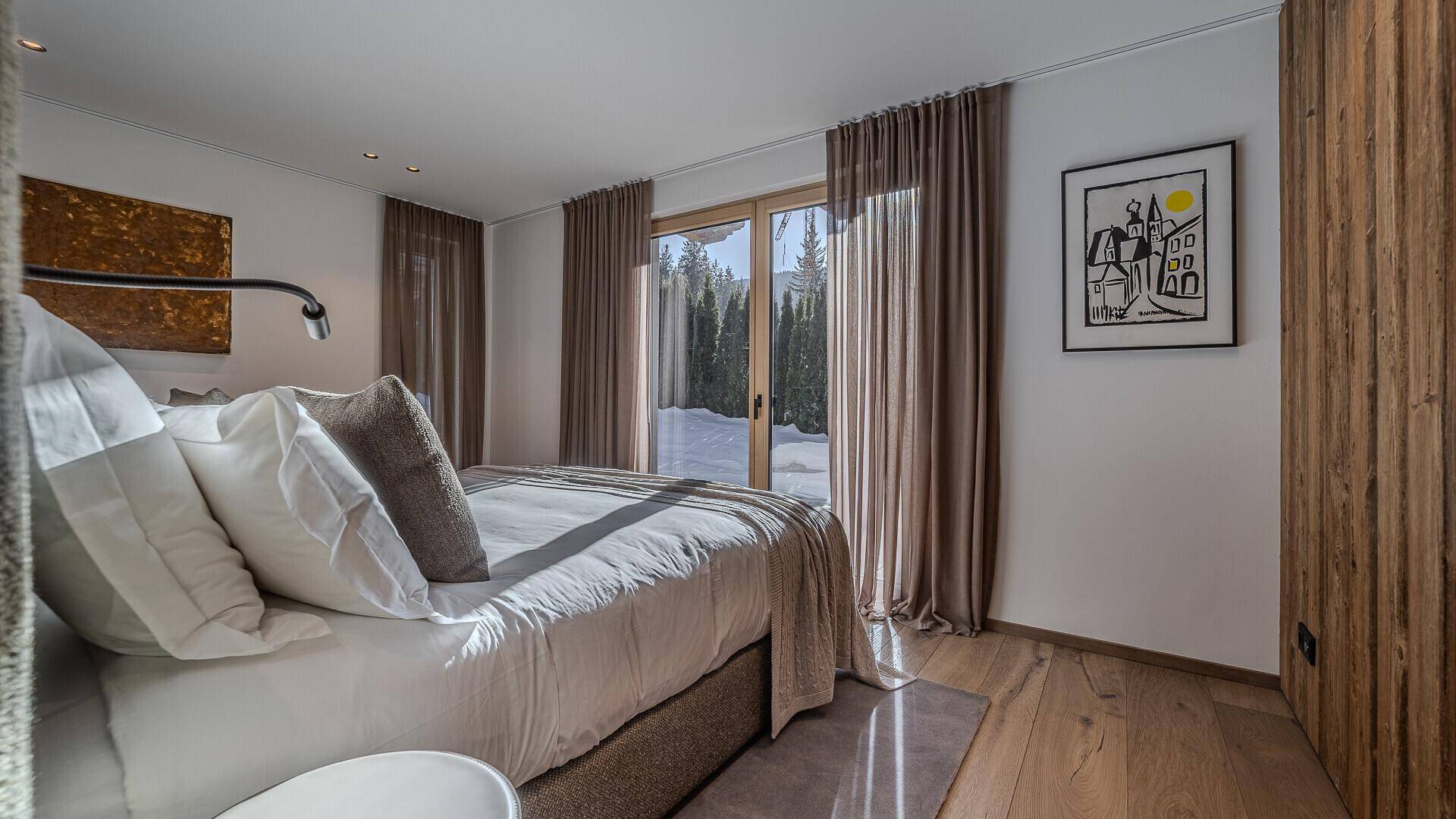 Helles Schlafzimmer mit Holzboden, Holzwand und Zugang zu einem Balkon mit Bergblick.