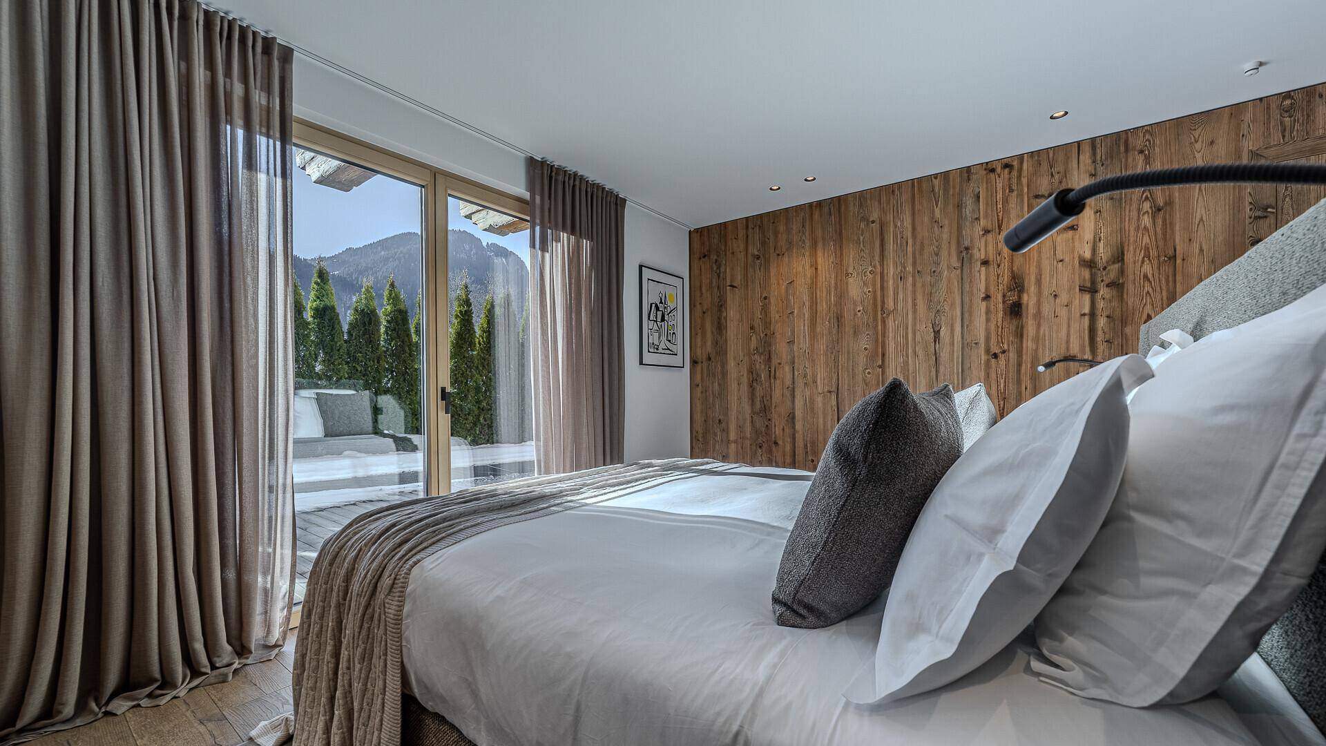 Gemütliches Schlafzimmer mit Holzwand, Holzboden und großen Fenstern mit Blick auf die Berge.
