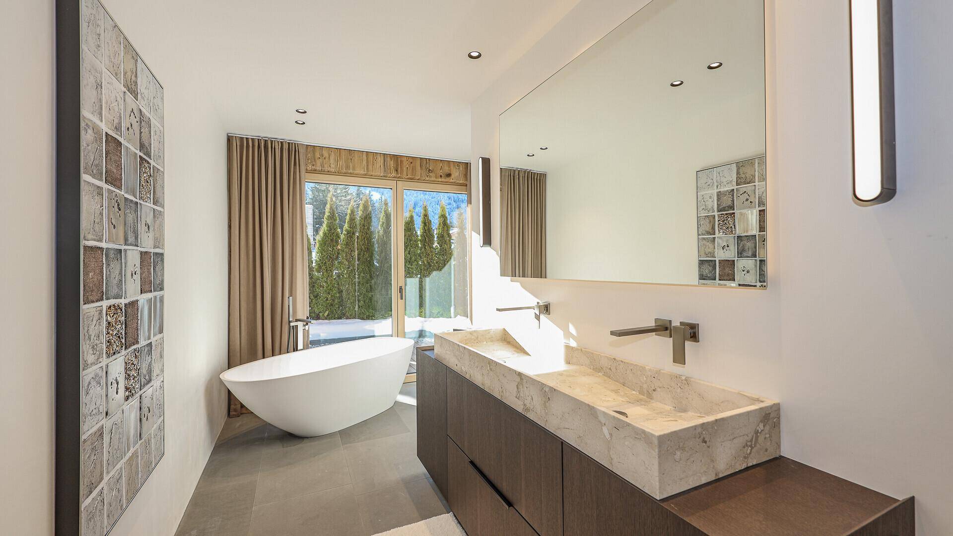 Elegantes Badezimmer mit freistehender Badewanne, Doppelwaschbecken und Zugang zum Außenbereich.