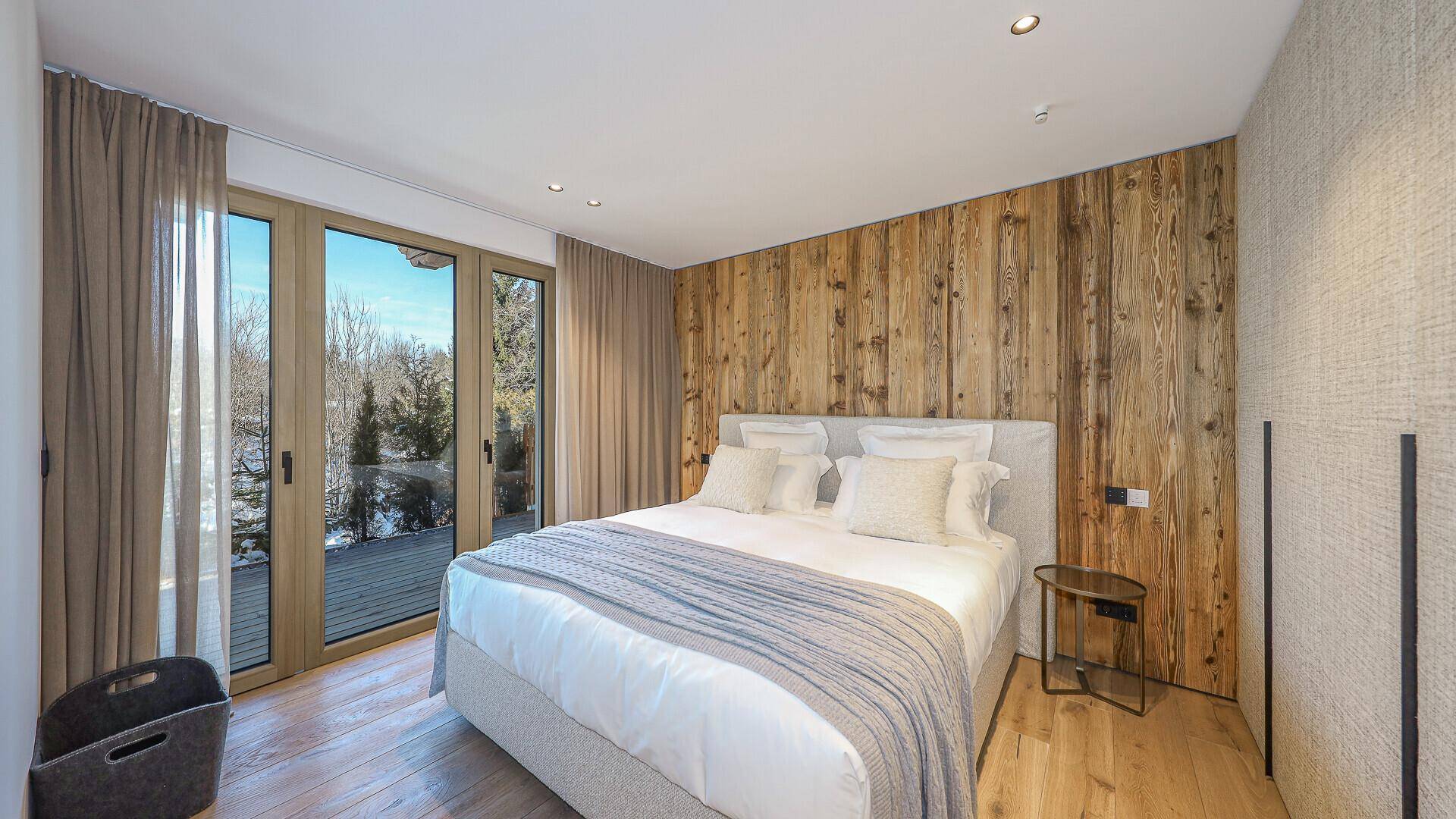 Helles Schlafzimmer mit Holzboden, Holzwand und Zugang zu einem Balkon mit Winterlandschaft.