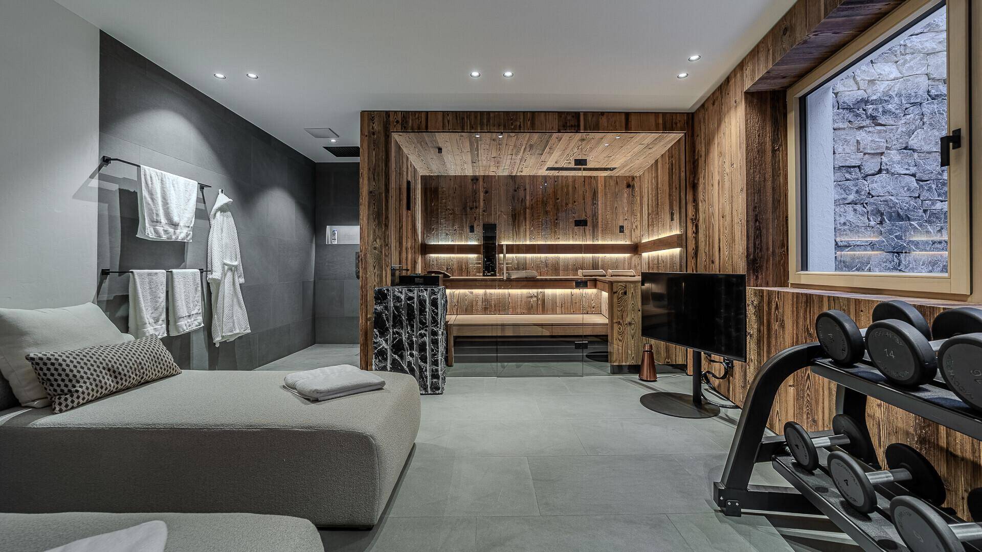 Modern gestalteter Wellnessbereich mit Sauna, Liegen und Hanteln für Entspannung und Training.