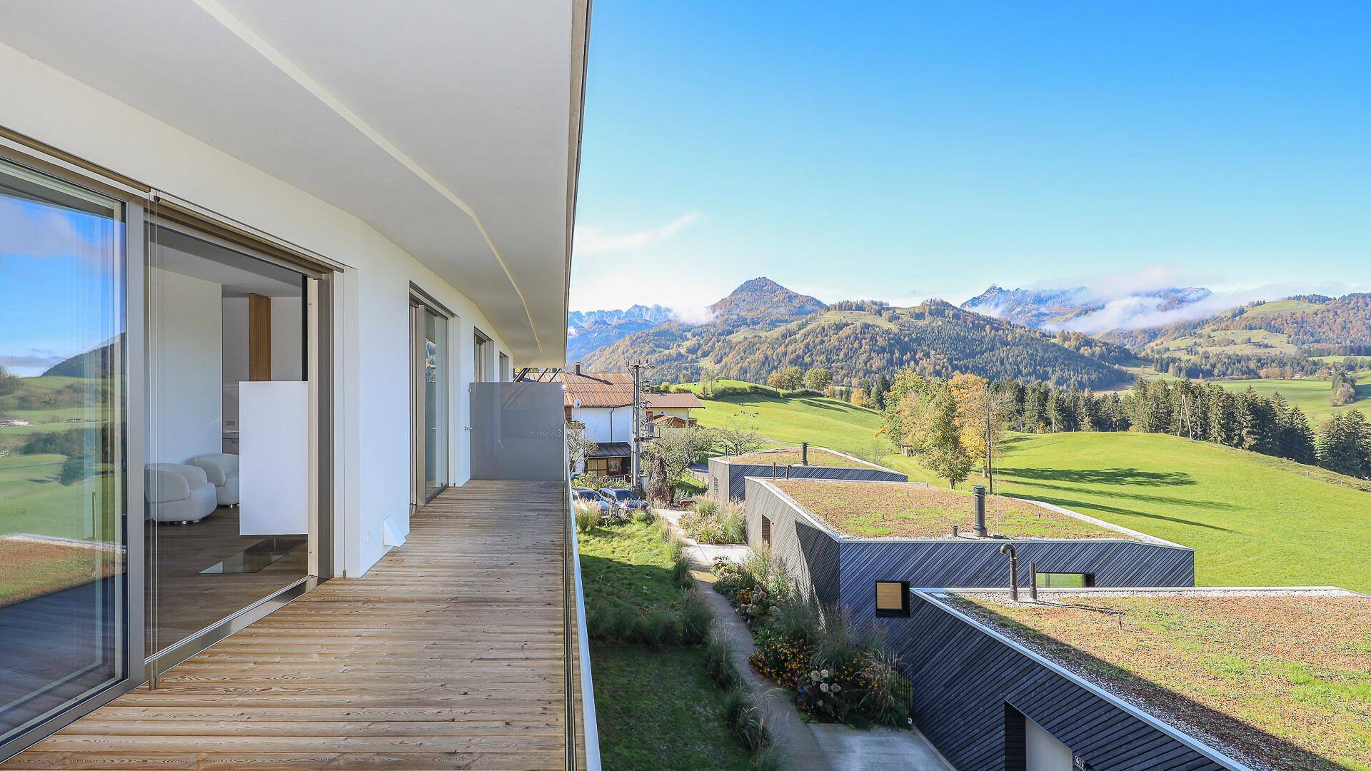 Langer Holzbalkon mit Glasgeländer und weitem Blick auf die grüne Berglandschaft.