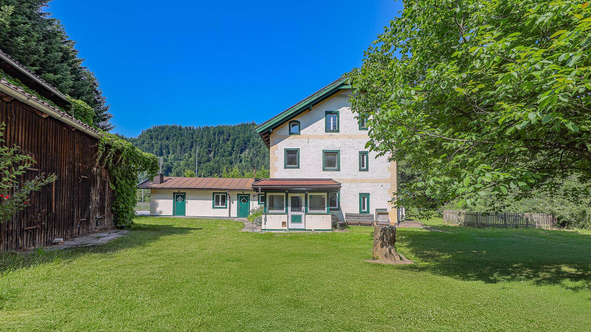 Ländliches Anwesen mit Haupthaus und Nebengebäude, umgeben von gepflegtem Rasen und Bäumen.