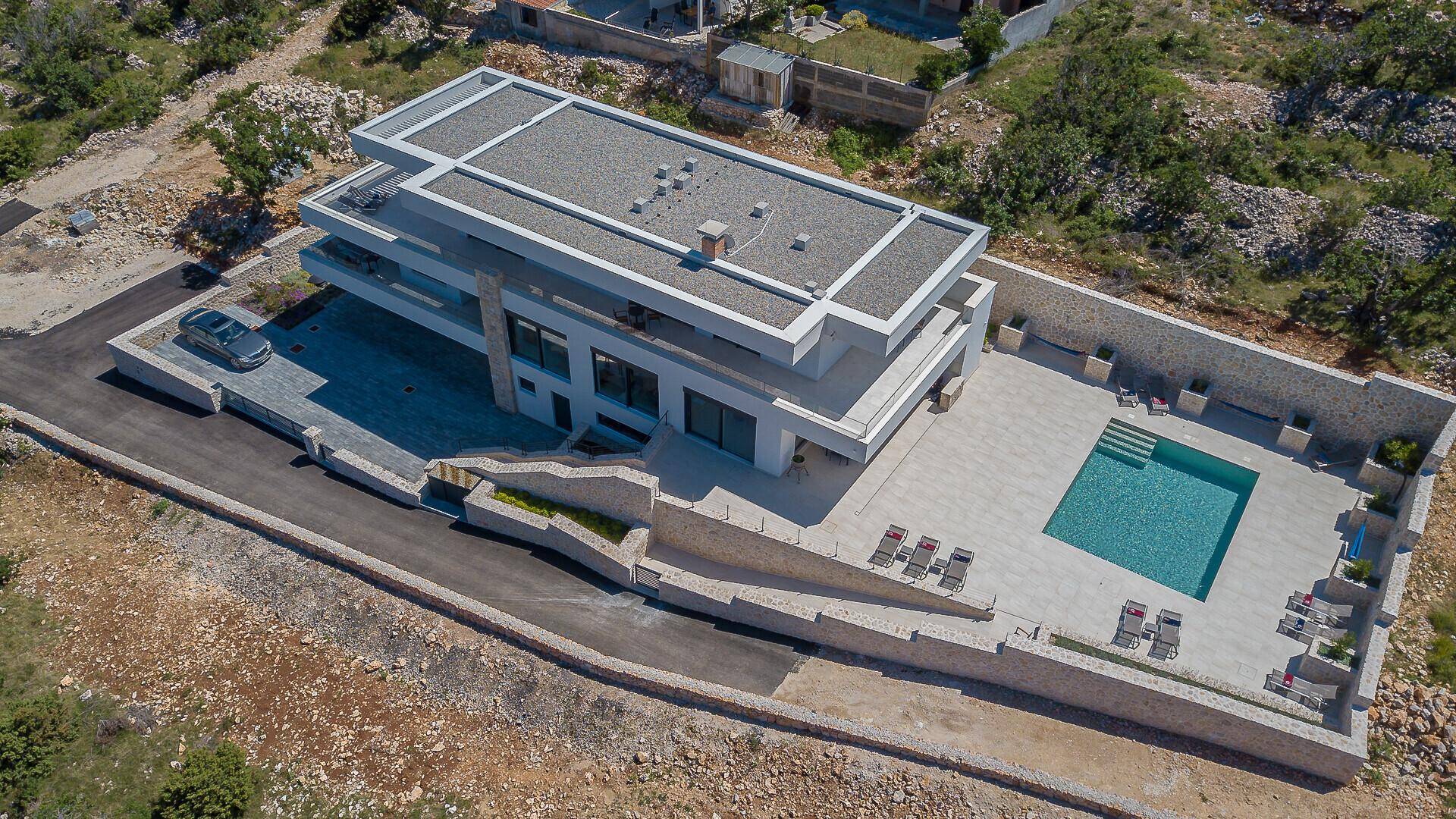 Luftaufnahme der modernen Villa mit Flachdach, großem Pool und weitläufigem Grundstück in Hanglage.