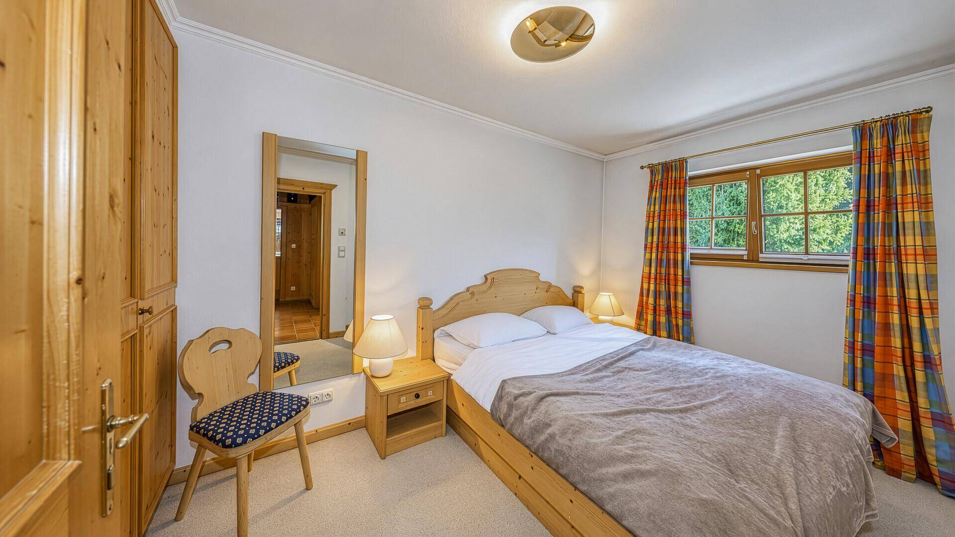 Gemütliches Schlafzimmer mit traditionellen Holzmöbeln, Teppichboden und einem Fenster mit Blick ins Grüne.